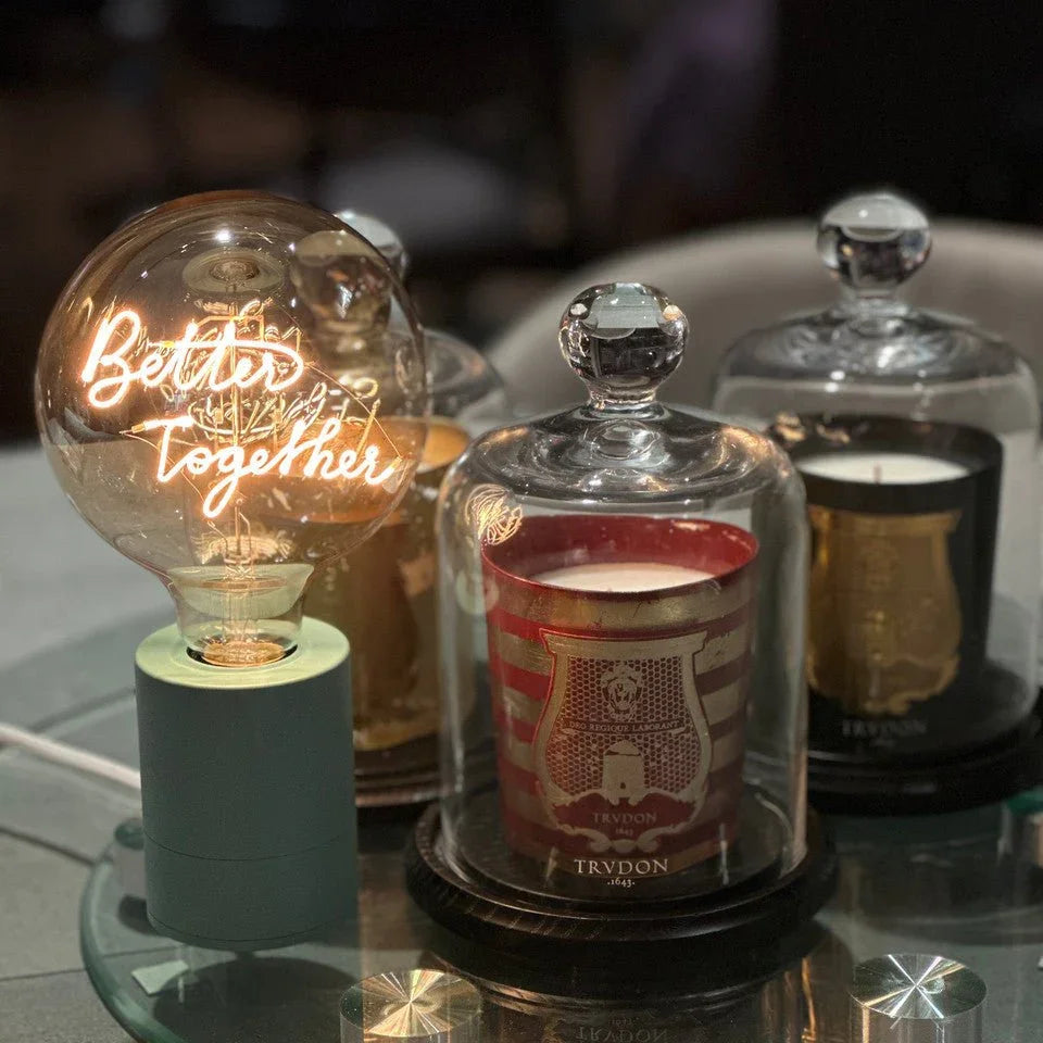 Ampoule LED à message lumineux 'Better Together' sur socle avec bougies décoratives sous cloche en verre.