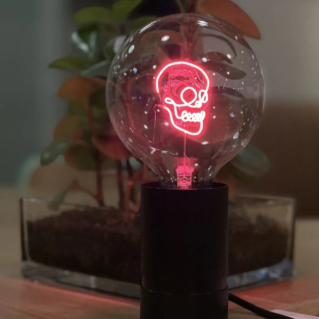 Ampoule LED design crâne lumineux rose sur socle noir, décor moderne, plante en arrière-plan