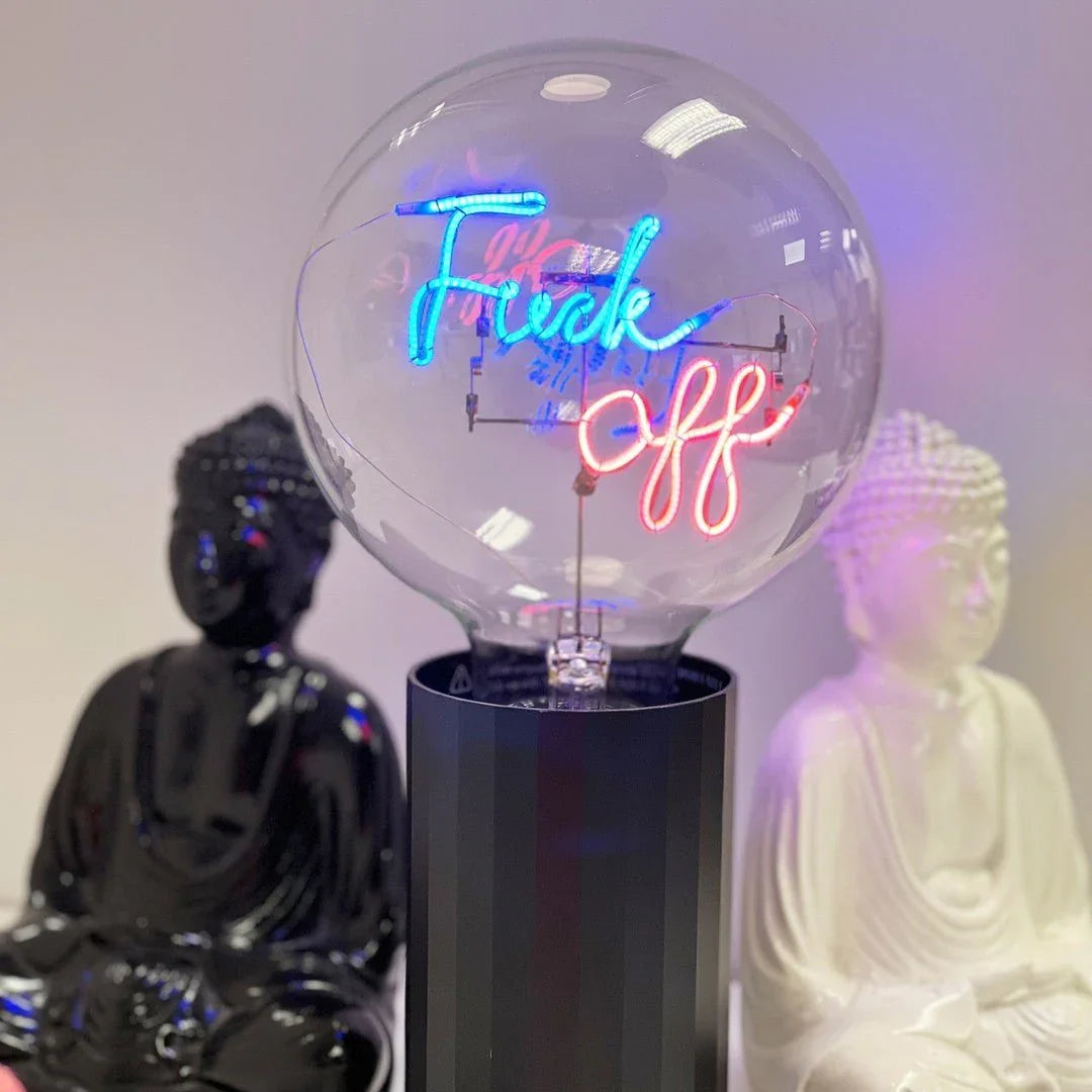 Ampoule LED design avec message néon coloré, posée entre deux statues de Bouddha