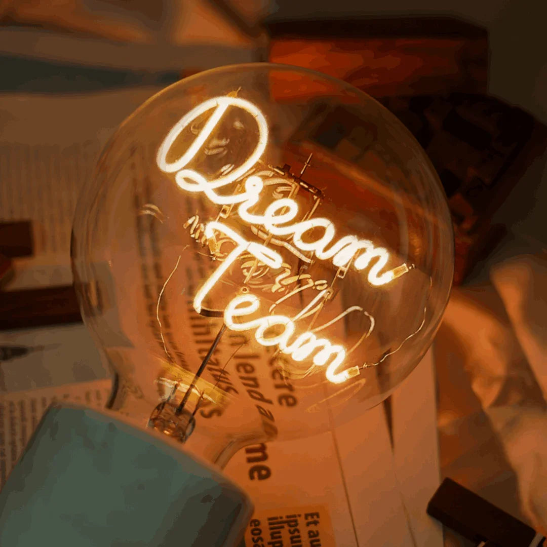 Ampoule LED design avec message lumineux « Dream Team » sur fond de journaux, ambiance chaleureuse